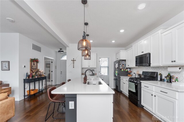 kitchen featuring sink, black appliances, a center island with sink, hanging light fixtures, and white cabinets