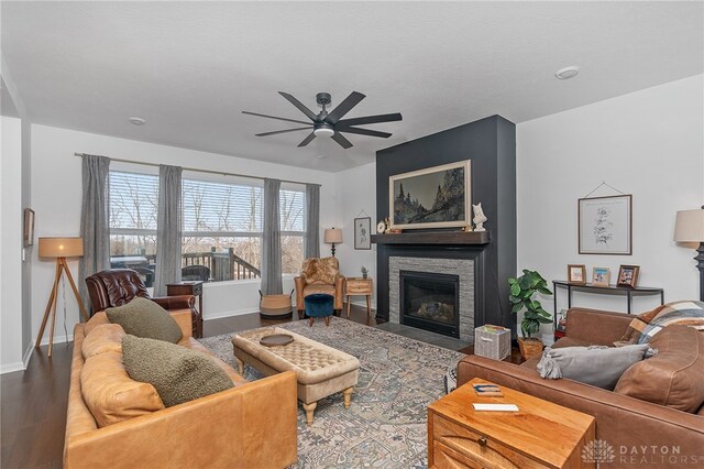 living room with ceiling fan, wood-type flooring, and a stone fireplace