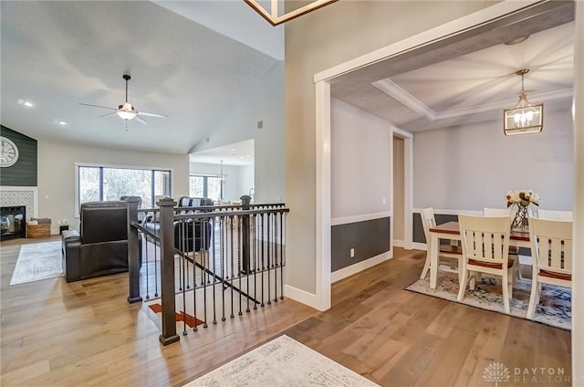 dining area featuring vaulted ceiling, ceiling fan with notable chandelier, hardwood / wood-style flooring, a tiled fireplace, and ornamental molding