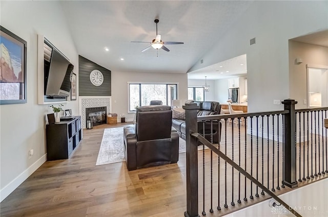 living room with hardwood / wood-style flooring, a tiled fireplace, ceiling fan with notable chandelier, and high vaulted ceiling