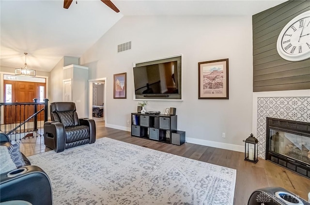 living room with ceiling fan, dark hardwood / wood-style floors, high vaulted ceiling, and a tile fireplace