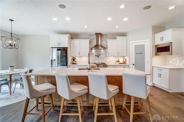 kitchen with white cabinetry, appliances with stainless steel finishes, a kitchen island with sink, and wall chimney range hood