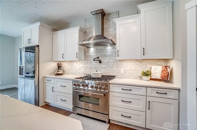 kitchen with wall chimney range hood, appliances with stainless steel finishes, backsplash, dark hardwood / wood-style floors, and white cabinets