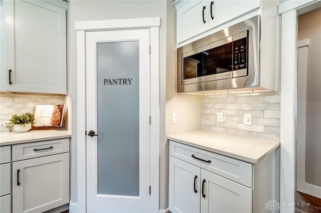 kitchen featuring white cabinetry, stainless steel microwave, light stone counters, and backsplash