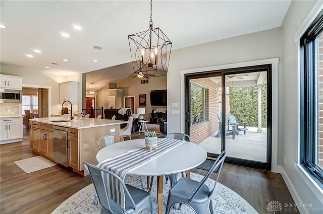 dining space with sink, ceiling fan with notable chandelier, and dark wood-type flooring