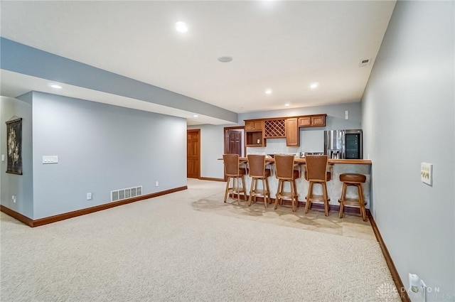 kitchen featuring light carpet, stainless steel fridge with ice dispenser, and a kitchen bar