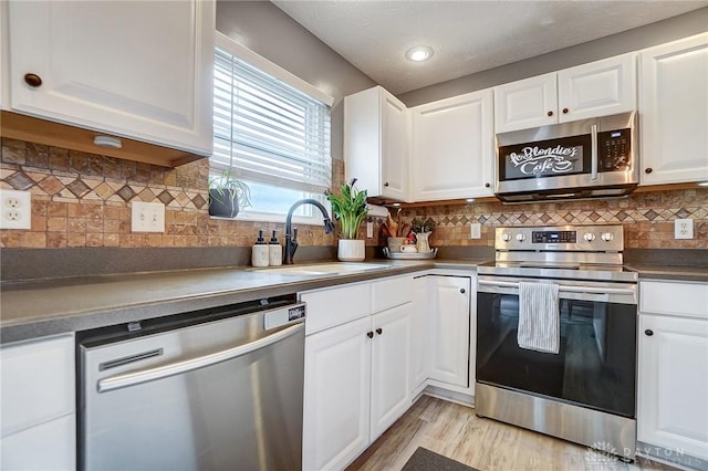 kitchen with sink, appliances with stainless steel finishes, white cabinetry, backsplash, and light hardwood / wood-style floors