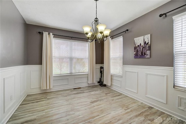 unfurnished dining area with plenty of natural light, a notable chandelier, and light wood-type flooring