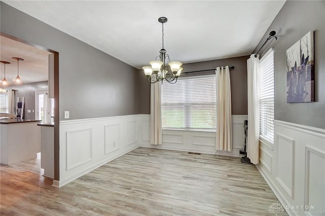 unfurnished dining area with a wealth of natural light, a chandelier, and light wood-type flooring