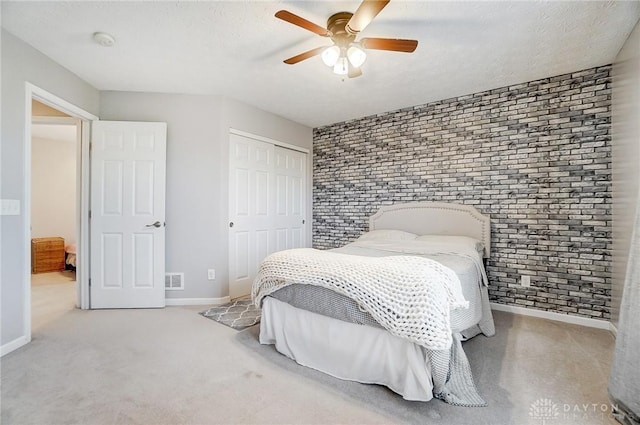 carpeted bedroom with ceiling fan, a closet, a textured ceiling, and brick wall