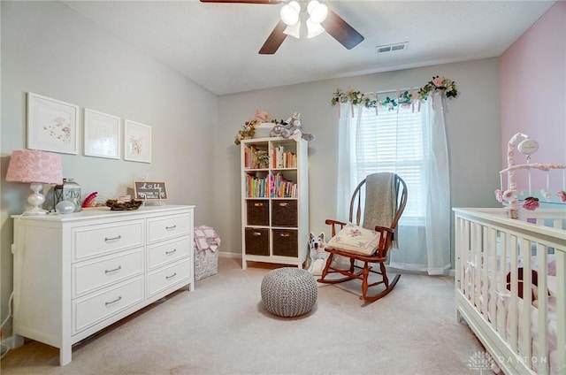 bedroom featuring a nursery area, ceiling fan, and light carpet