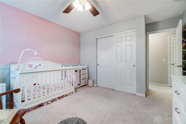 carpeted bedroom featuring ceiling fan, a closet, and a crib