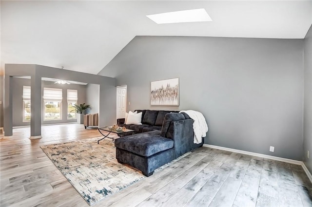 living room featuring ceiling fan, light hardwood / wood-style flooring, high vaulted ceiling, and a skylight