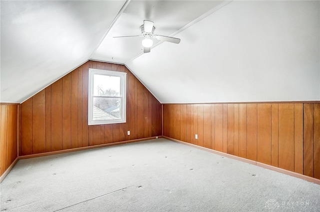 bonus room with vaulted ceiling, light colored carpet, ceiling fan, and wood walls