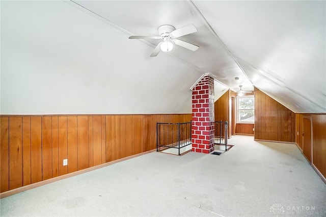 bonus room featuring ceiling fan, lofted ceiling, light carpet, and wood walls