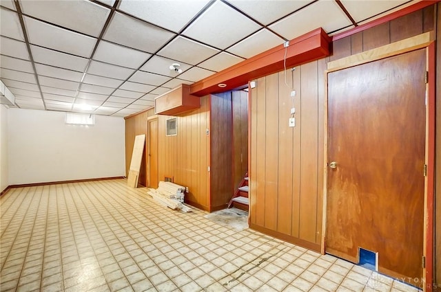 basement with a drop ceiling and wooden walls