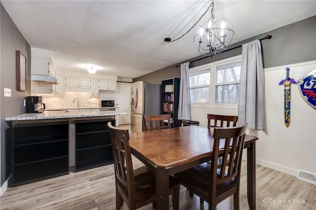 dining space with an inviting chandelier, light hardwood / wood-style floors, and sink