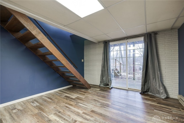 empty room featuring brick wall, wood-type flooring, floor to ceiling windows, and a drop ceiling