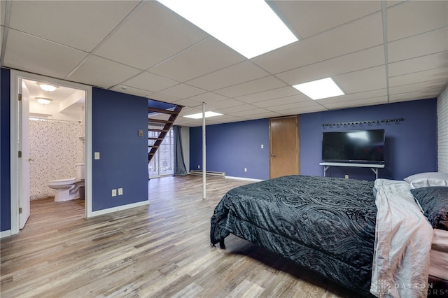 bedroom featuring connected bathroom, hardwood / wood-style floors, a paneled ceiling, and a baseboard heating unit