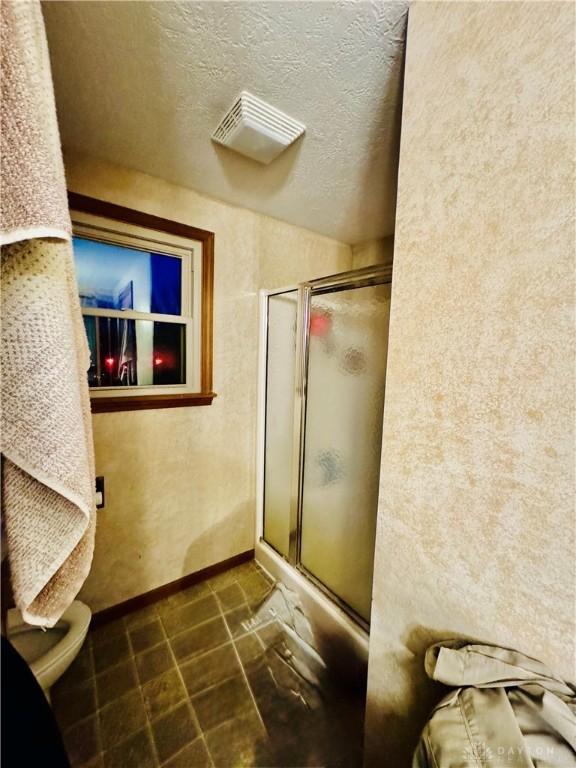 bathroom featuring an enclosed shower, a textured ceiling, tile patterned floors, and toilet