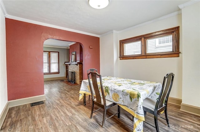 dining space featuring wood-type flooring, a brick fireplace, and ornamental molding