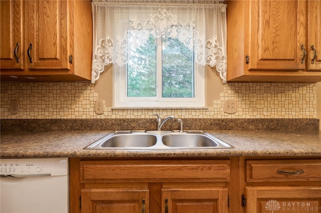 kitchen featuring dark countertops, white dishwasher, a sink, and brown cabinets