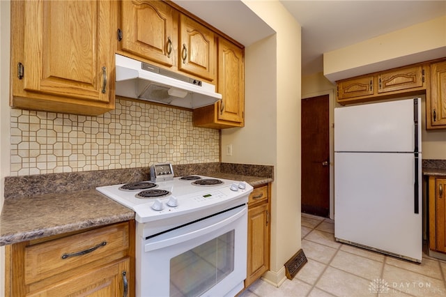 kitchen with white appliances, dark countertops, brown cabinets, and under cabinet range hood