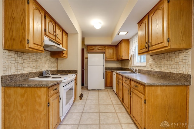 kitchen with brown cabinets, dark countertops, a sink, white appliances, and under cabinet range hood