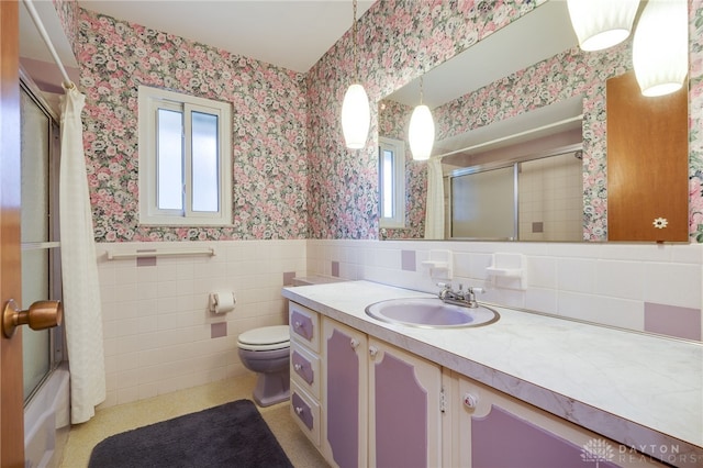 bathroom with toilet, a wainscoted wall, vanity, tile walls, and wallpapered walls