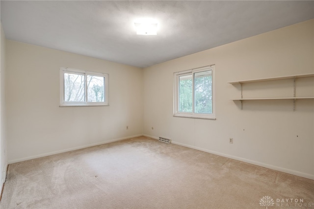 unfurnished room with light carpet, baseboards, visible vents, and a wealth of natural light