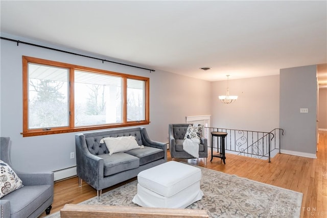 living area featuring baseboards, light wood finished floors, baseboard heating, and an inviting chandelier