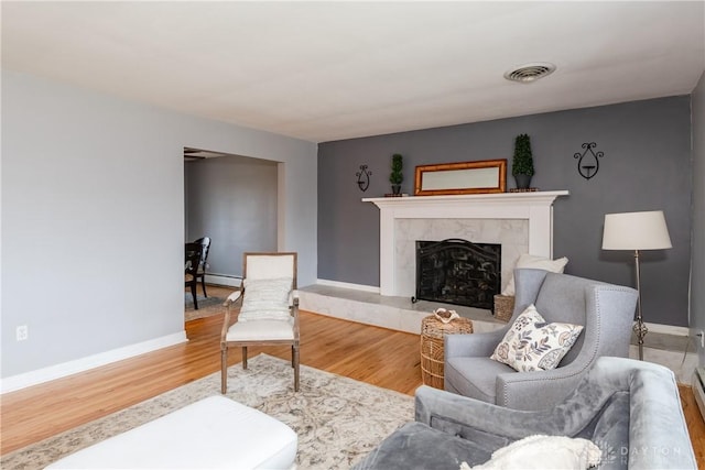 living room with a baseboard heating unit, wood finished floors, visible vents, and a premium fireplace