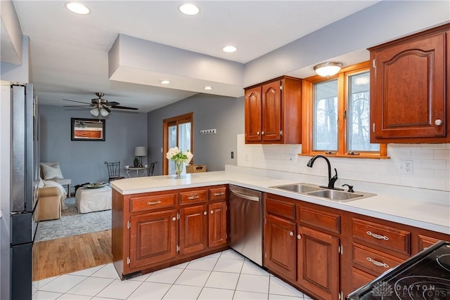 kitchen featuring stainless steel appliances, tasteful backsplash, light countertops, a sink, and a peninsula