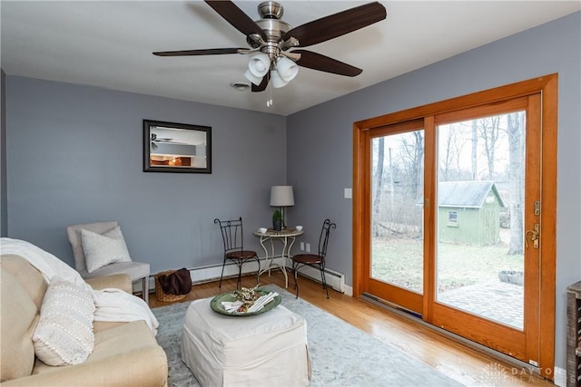 living area featuring ceiling fan, baseboards, baseboard heating, and wood finished floors