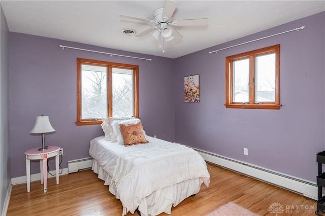 bedroom with light wood finished floors, multiple windows, and a baseboard radiator