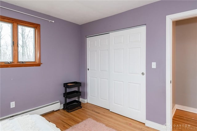 bedroom featuring light wood finished floors, baseboards, a baseboard heating unit, and a closet