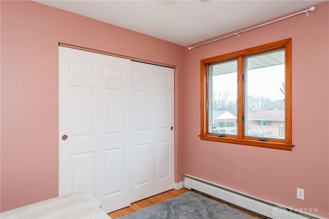 bedroom featuring light wood-type flooring, baseboards, baseboard heating, and a closet