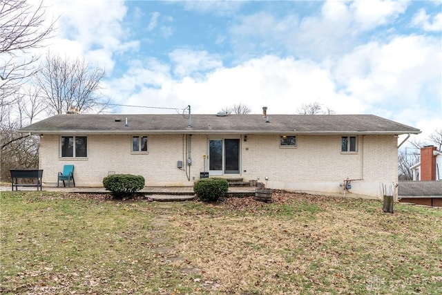 back of house featuring entry steps, a patio, brick siding, and a lawn