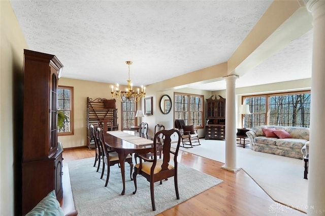 dining area with a textured ceiling, decorative columns, a chandelier, and light wood-type flooring