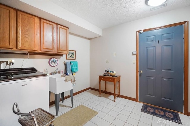 laundry room with light tile patterned floors, washing machine and dryer, cabinets, and a textured ceiling