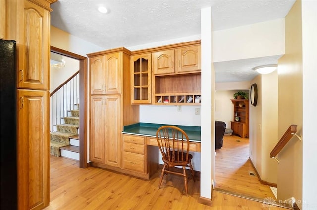 kitchen with black refrigerator, built in desk, light hardwood / wood-style floors, and a textured ceiling