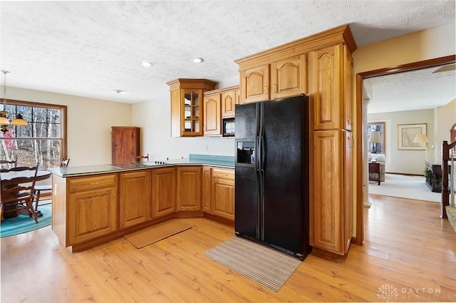 kitchen with decorative light fixtures, kitchen peninsula, light hardwood / wood-style floors, and black appliances