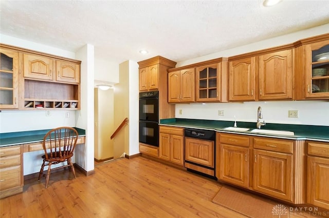 kitchen featuring sink, built in desk, black double oven, light hardwood / wood-style floors, and paneled dishwasher