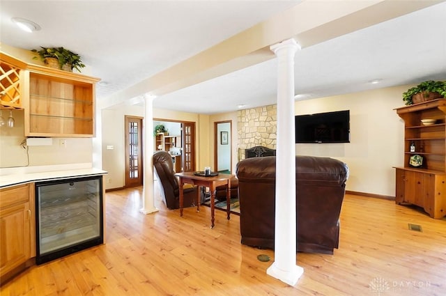 living room with light hardwood / wood-style flooring, decorative columns, beverage cooler, and indoor bar