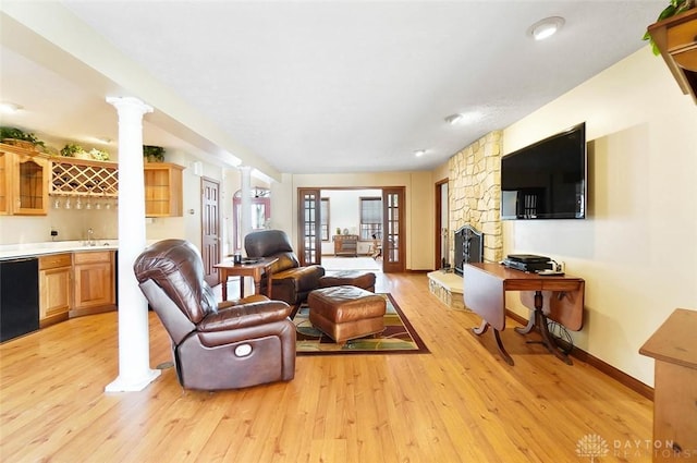 living room featuring decorative columns, a stone fireplace, wet bar, and light hardwood / wood-style floors