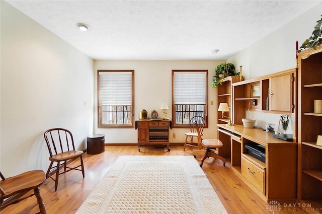 sitting room featuring built in desk, light hardwood / wood-style flooring, and a textured ceiling