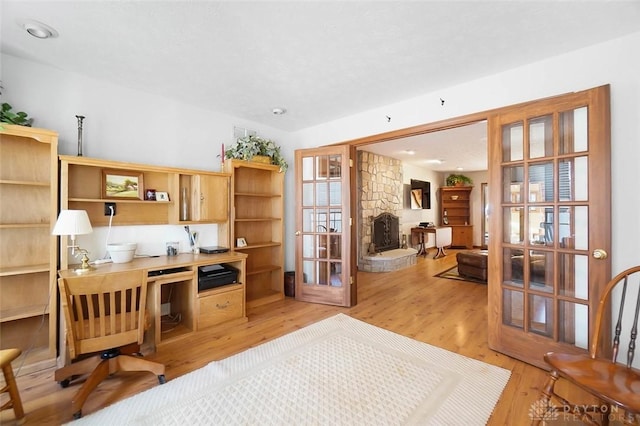 home office with a stone fireplace, light hardwood / wood-style flooring, and french doors