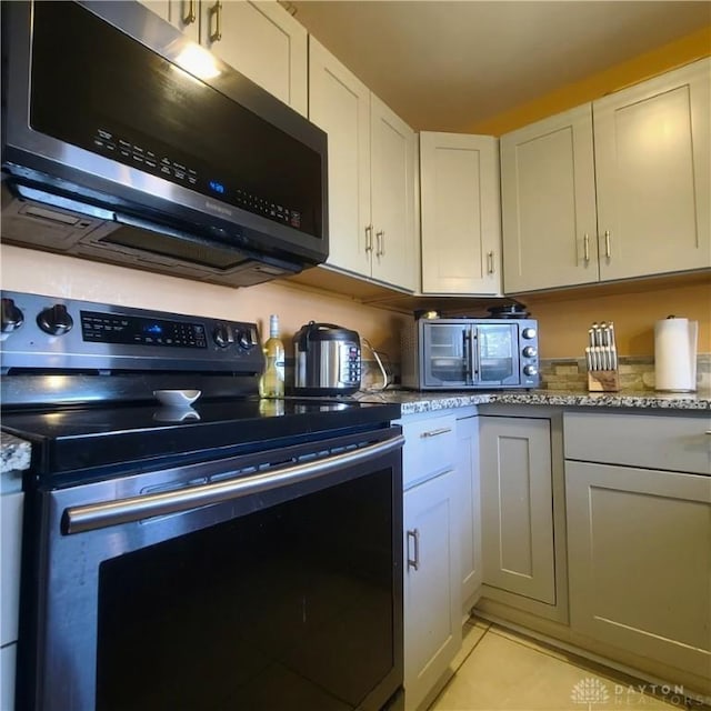 kitchen with appliances with stainless steel finishes, light tile patterned floors, white cabinets, and light stone counters