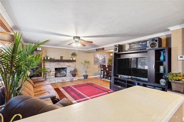 living room with hardwood / wood-style flooring, ceiling fan, ornamental molding, and a fireplace