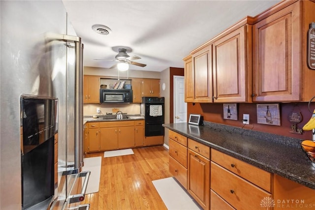 kitchen featuring dark stone countertops, light hardwood / wood-style flooring, ceiling fan, and black appliances